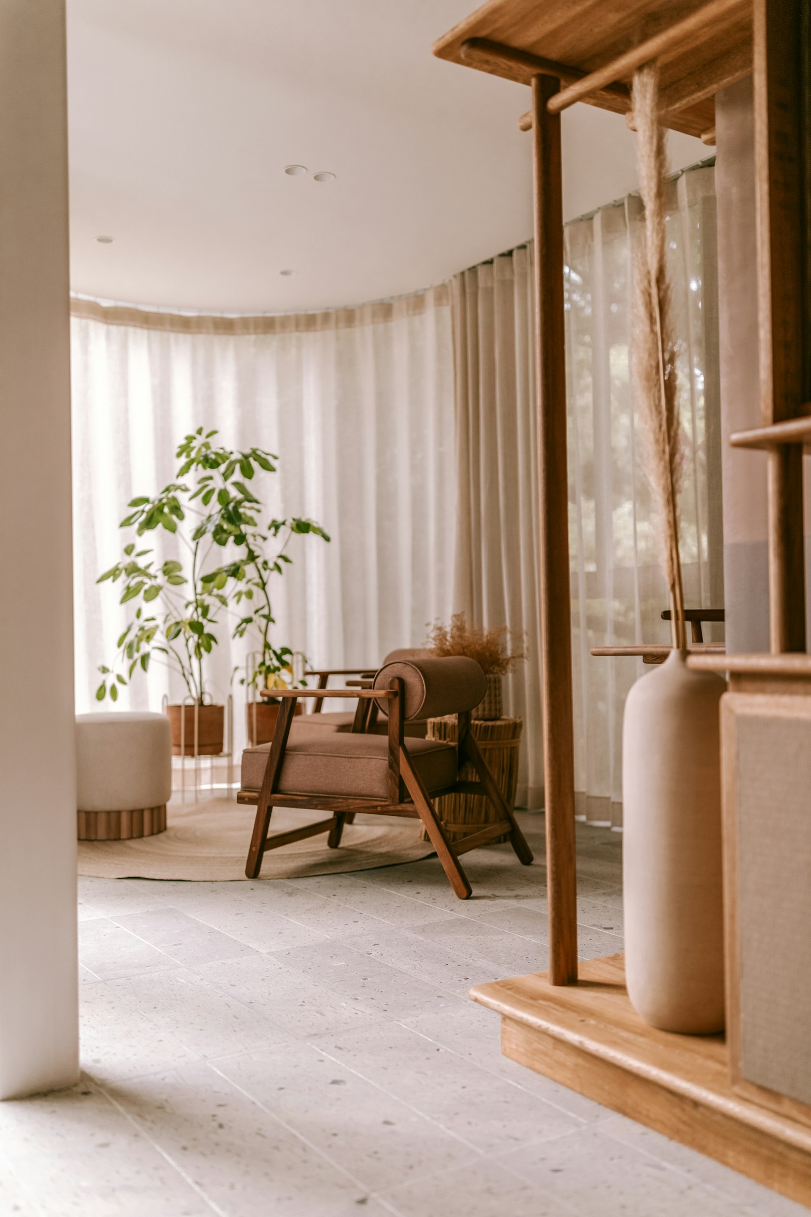 Sunlit boutique hotel lounge with linen curtains, a wooden armchair and a ceramic vase
