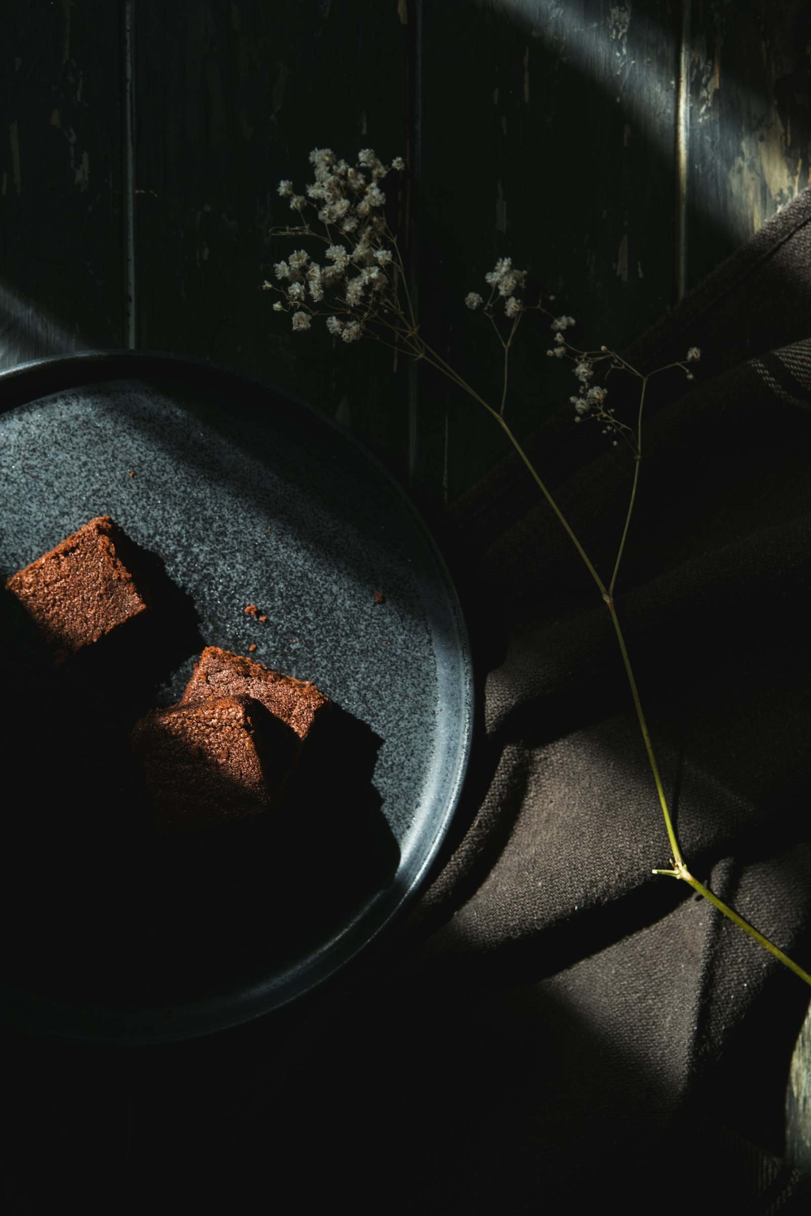 Chocolate dessert on a dark stoneware plate with a dried flower sprig